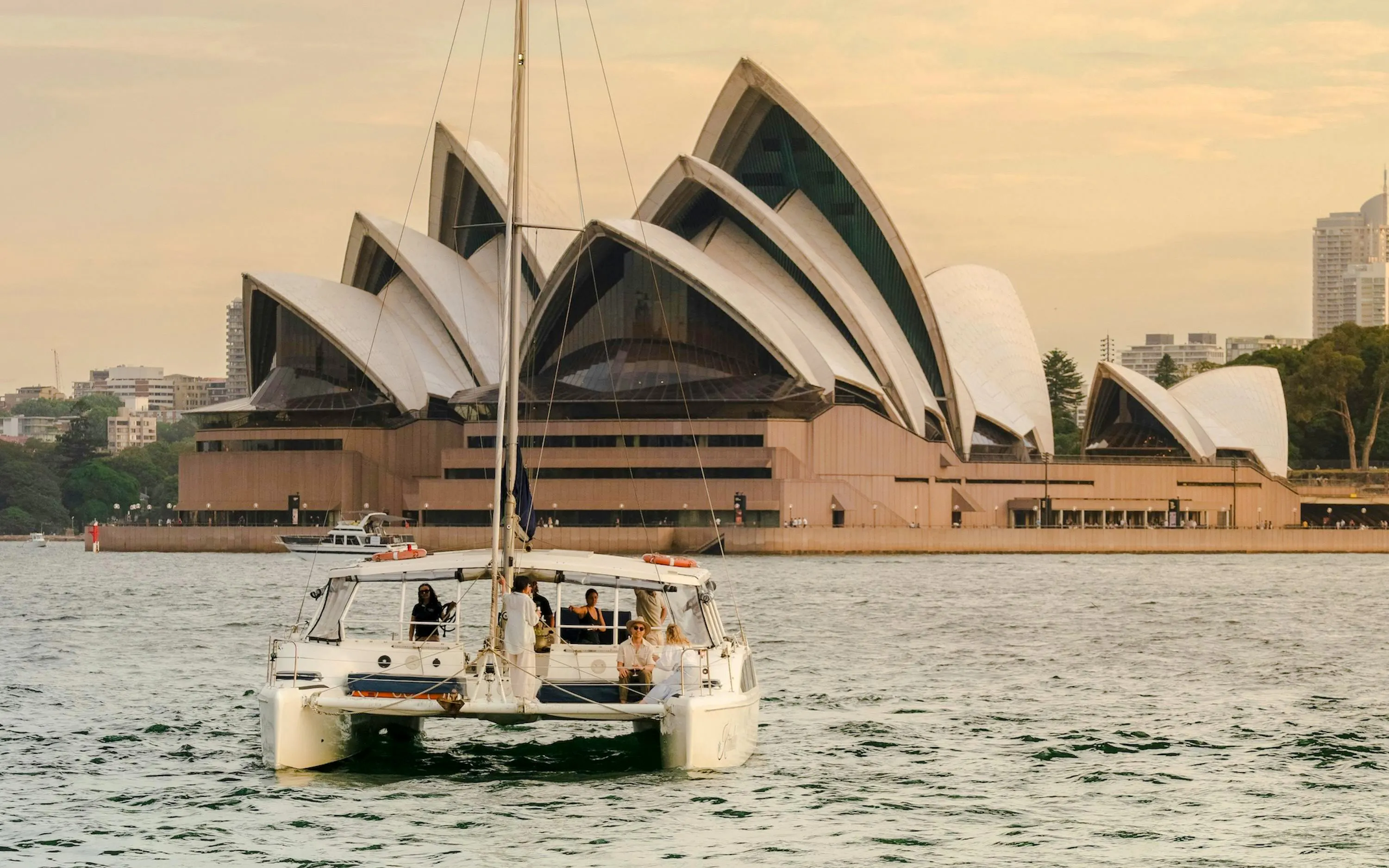 Catamaran sailing near Sydney Opera House at sunset.