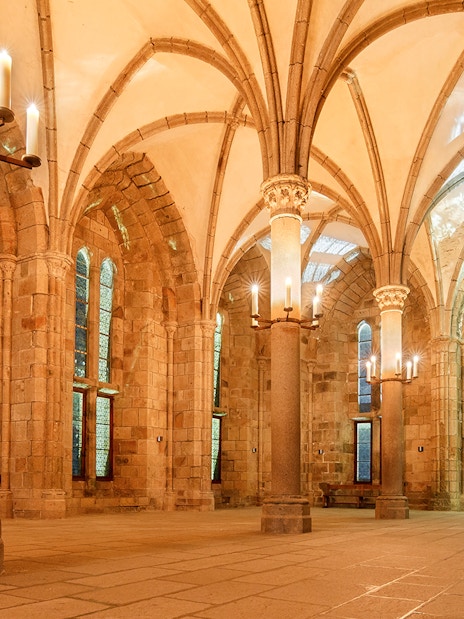 Mont St. Michel Abbey interior with vaulted ceilings and candlelit columns.