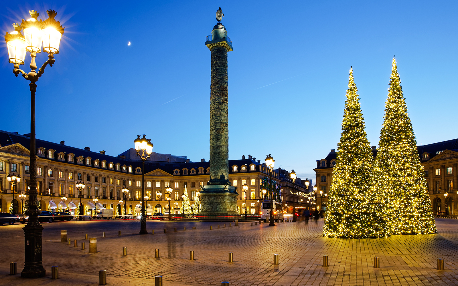 Place Vendôme in Paris with illuminated Christmas trees and Vendôme Column at dusk.