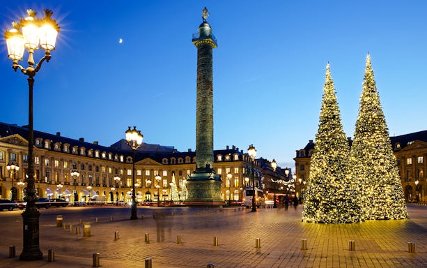 Place Vendôme in Paris with illuminated Christmas trees and Vendôme Column at dusk.