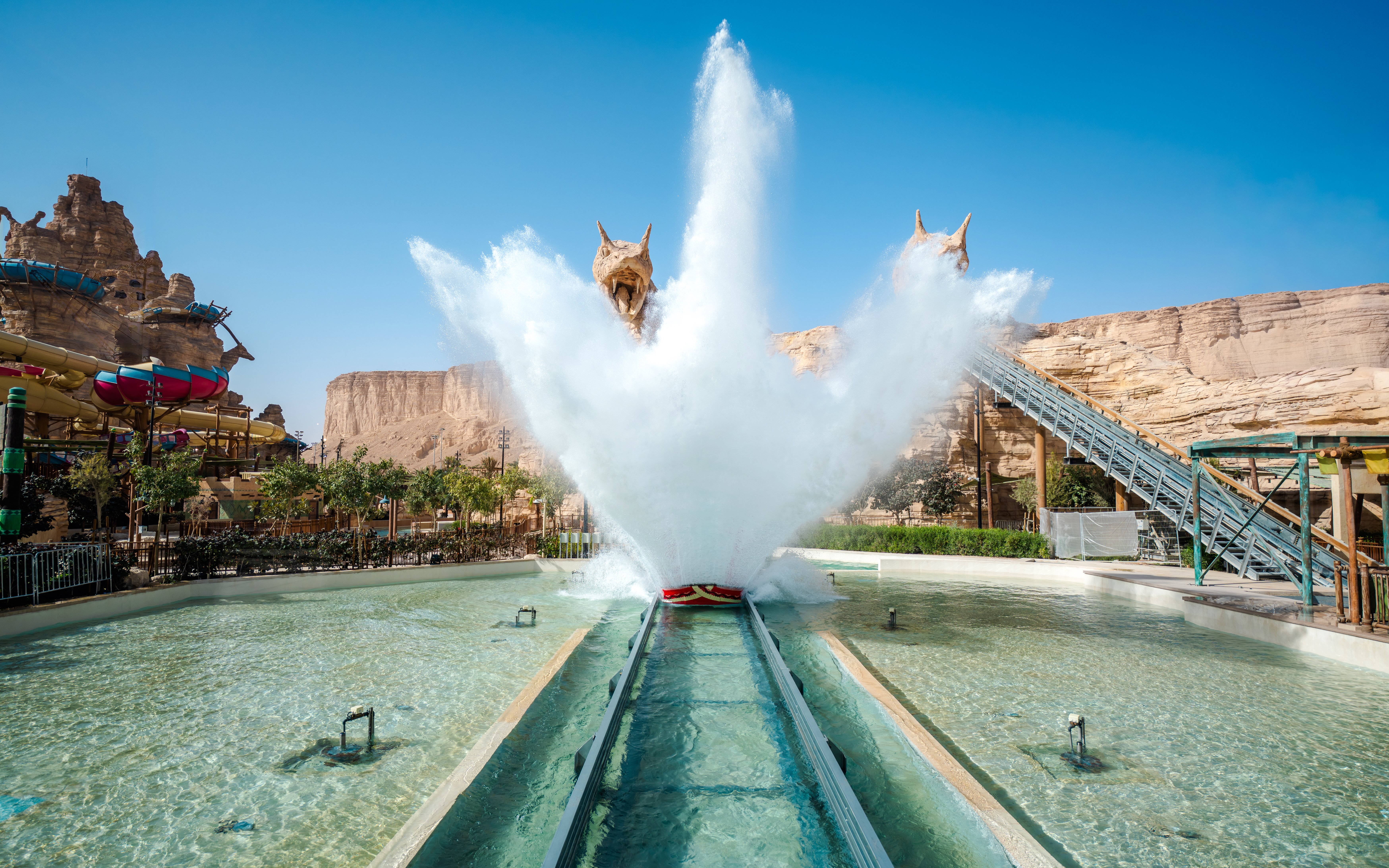 Water ride splash at Aquarabia Qiddiya with rocky backdrop and colorful slides.