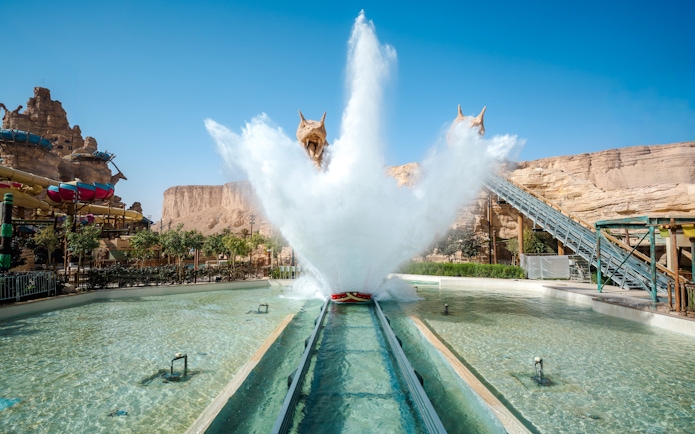 Water ride splash at Aquarabia Qiddiya with rocky backdrop and colorful slides.