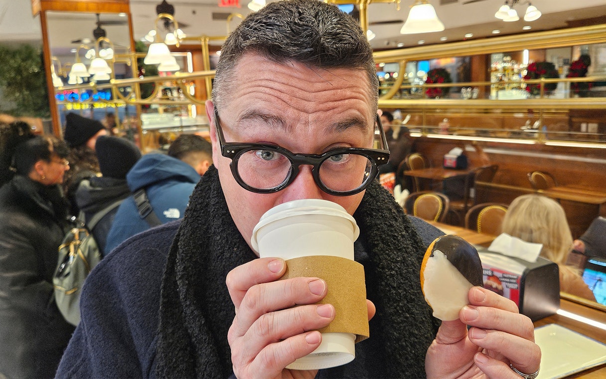 Man enjoying coffee and a black-and-white cookie in a New York café during Christmas Lights Bus Tour.