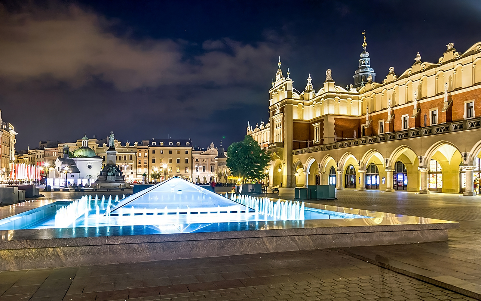 Krakow's Rynek Underground Museum entrance with illuminated fountain at night.