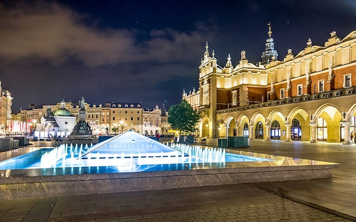 Krakow's Rynek Underground Museum entrance with illuminated fountain at night.