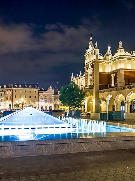 Krakow's Rynek Underground Museum entrance with illuminated fountain at night.