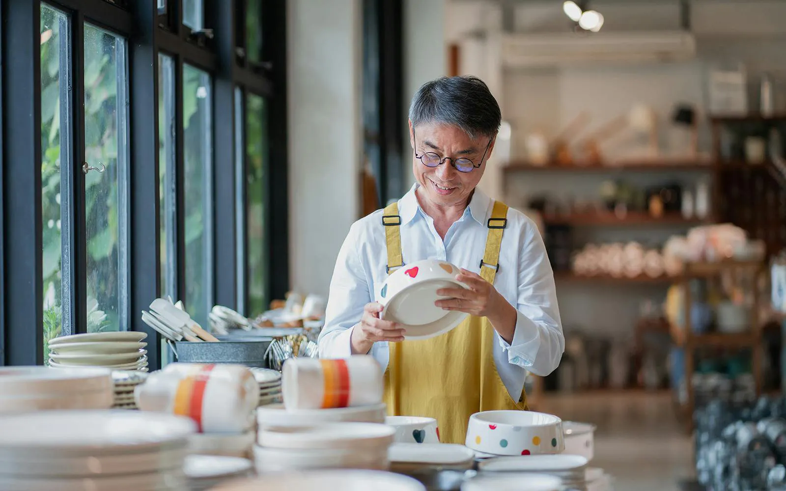 Senior Asian shop owner examining a handmade ceramic plate in his store.