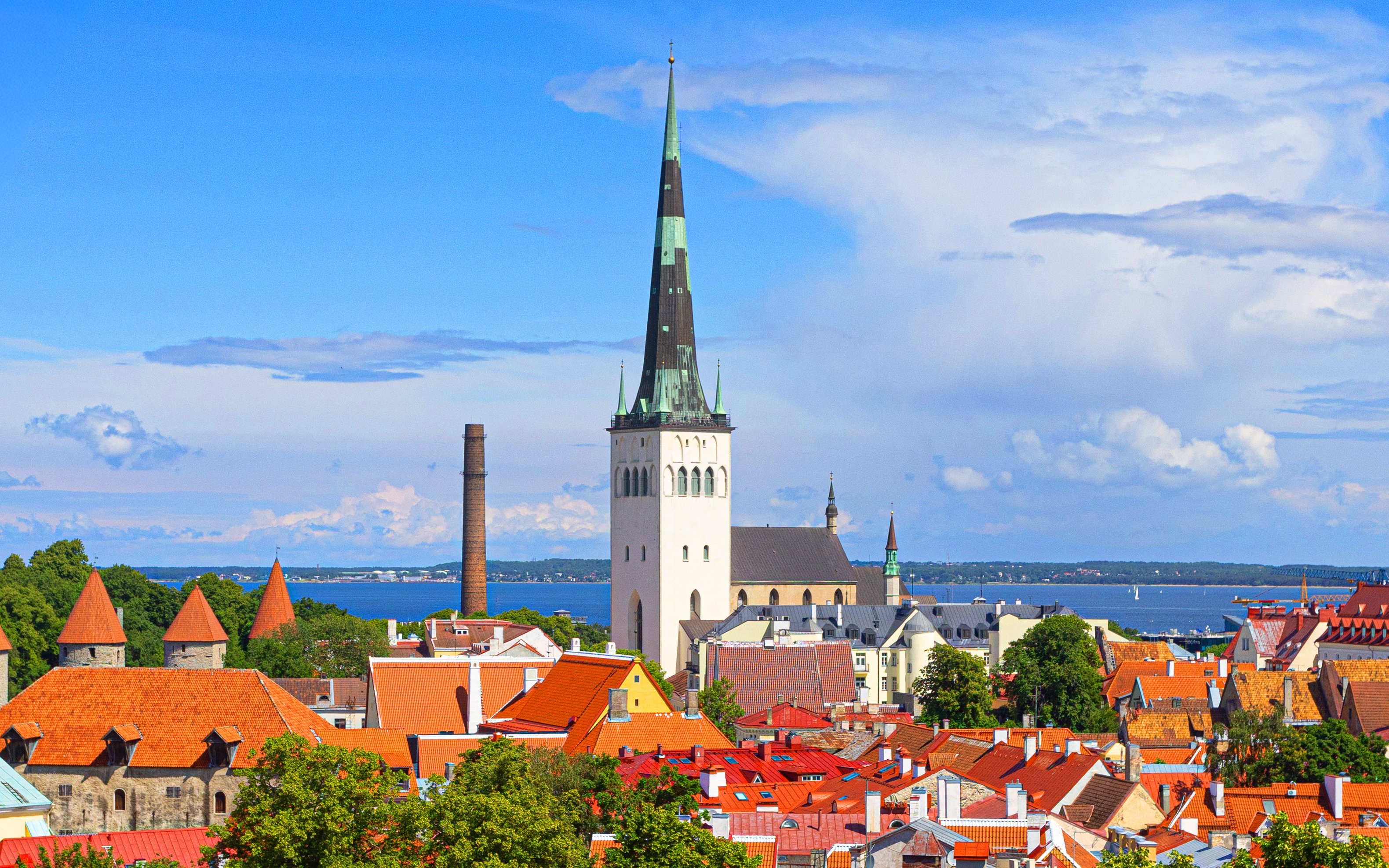 Tallinn old town with St. Olaf's Church spire and red rooftops against a blue sky.