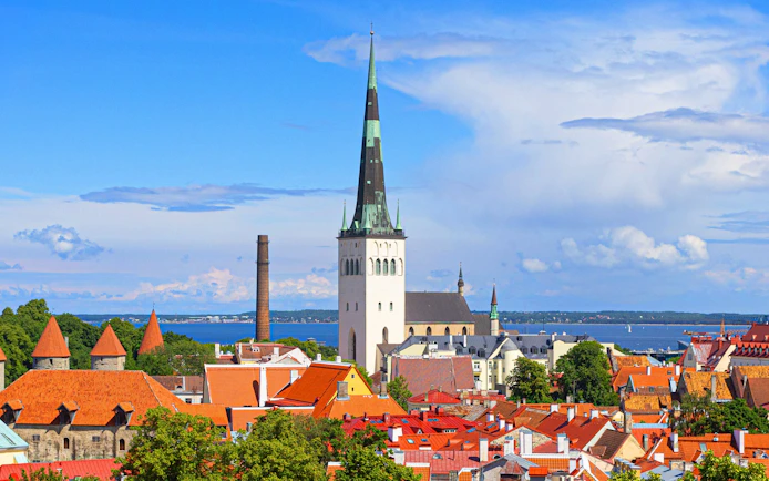 Tallinn old town with St. Olaf's Church spire and red rooftops against a blue sky.