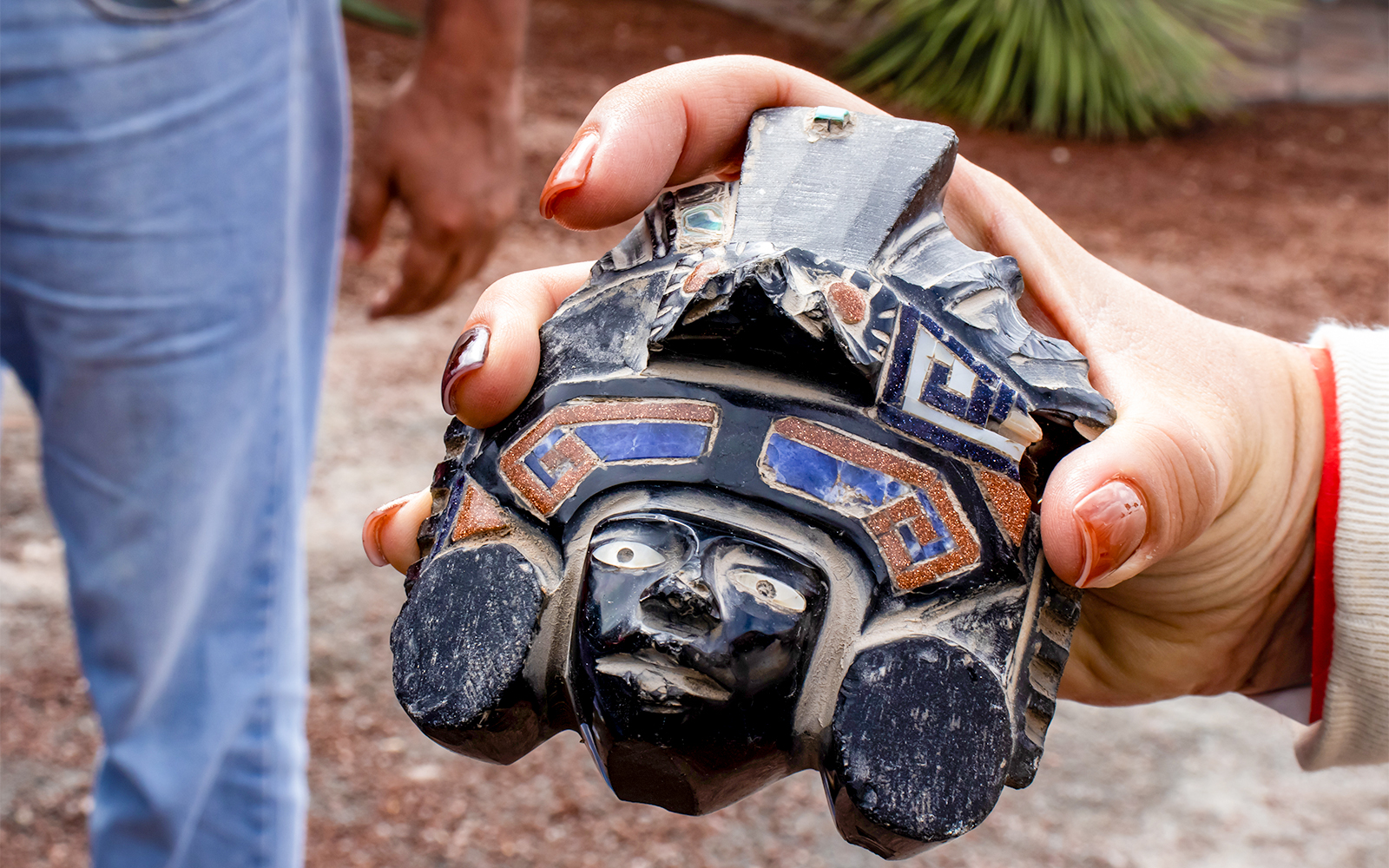 Tourist guide presenting obsidian handcraft to visitors at Teotihuacan archaeological site.