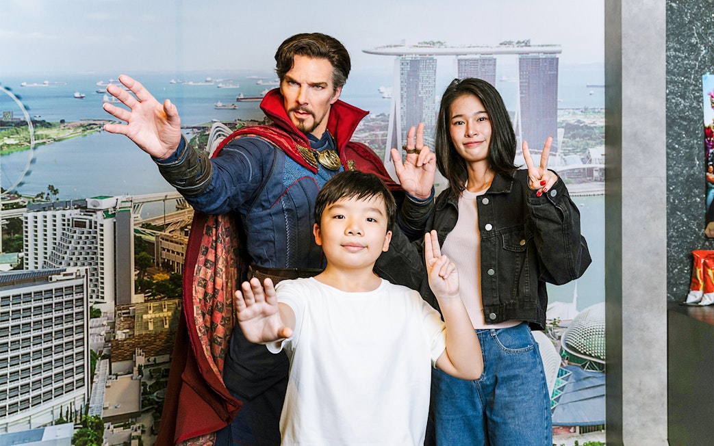 Wax figure of a superhero with visitors at Madame Tussauds Singapore, Marina Bay Sands backdrop.