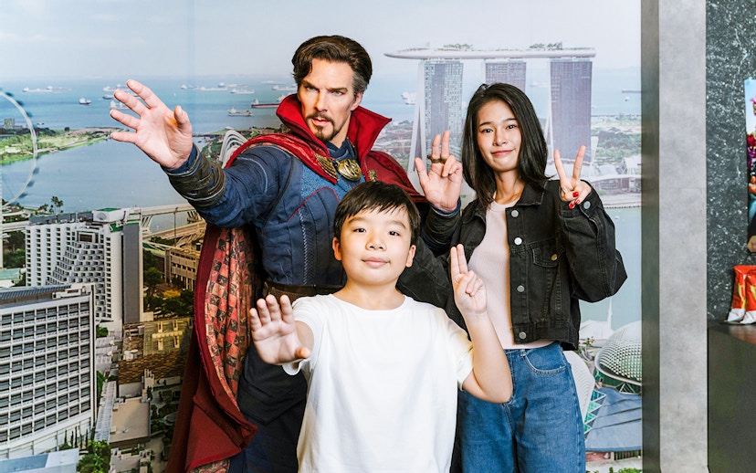 Wax figure of a superhero with visitors at Madame Tussauds Singapore, Marina Bay Sands backdrop.