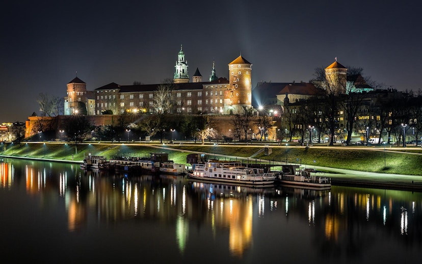 Wawel Castle illuminated at night, reflected in the Vistula River during a night cruise in Krakow, Poland.