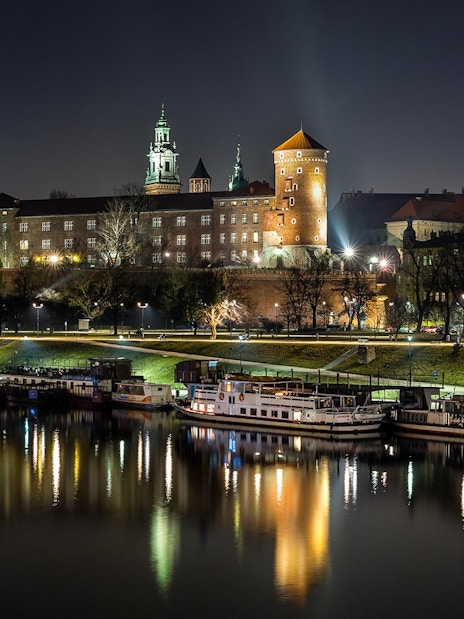 Wawel Castle illuminated at night, reflected in the Vistula River during a night cruise in Krakow, Poland.