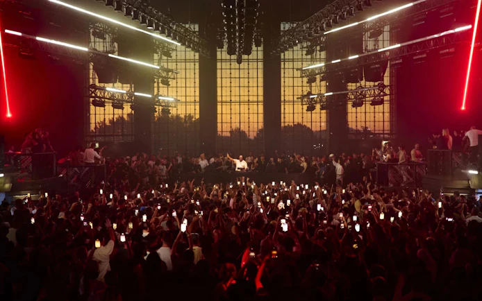 DJ performing at a packed Ibiza venue with vibrant lights and sunset backdrop.