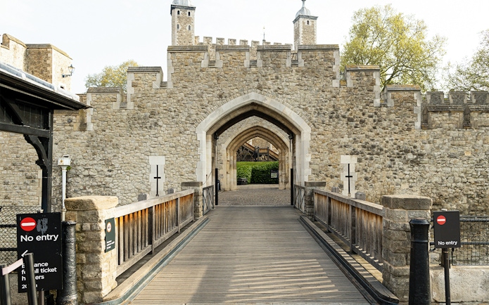 Tower of London entrance gate with stone walls and wooden bridge.