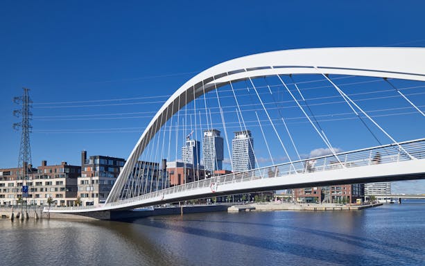 Modern bridge spanning water in Kalasatama district, Helsinki, with cityscape in background.