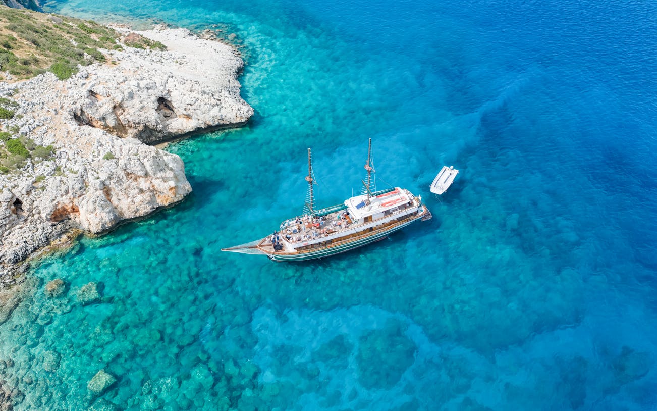Cruise ship near rocky coast in Blue Lagoon, Cyprus, with clear turquoise water.