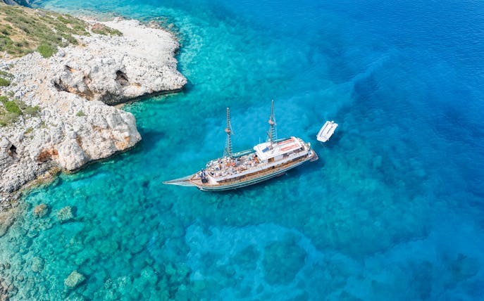Cruise ship near rocky coast in Blue Lagoon, Cyprus, with clear turquoise water.