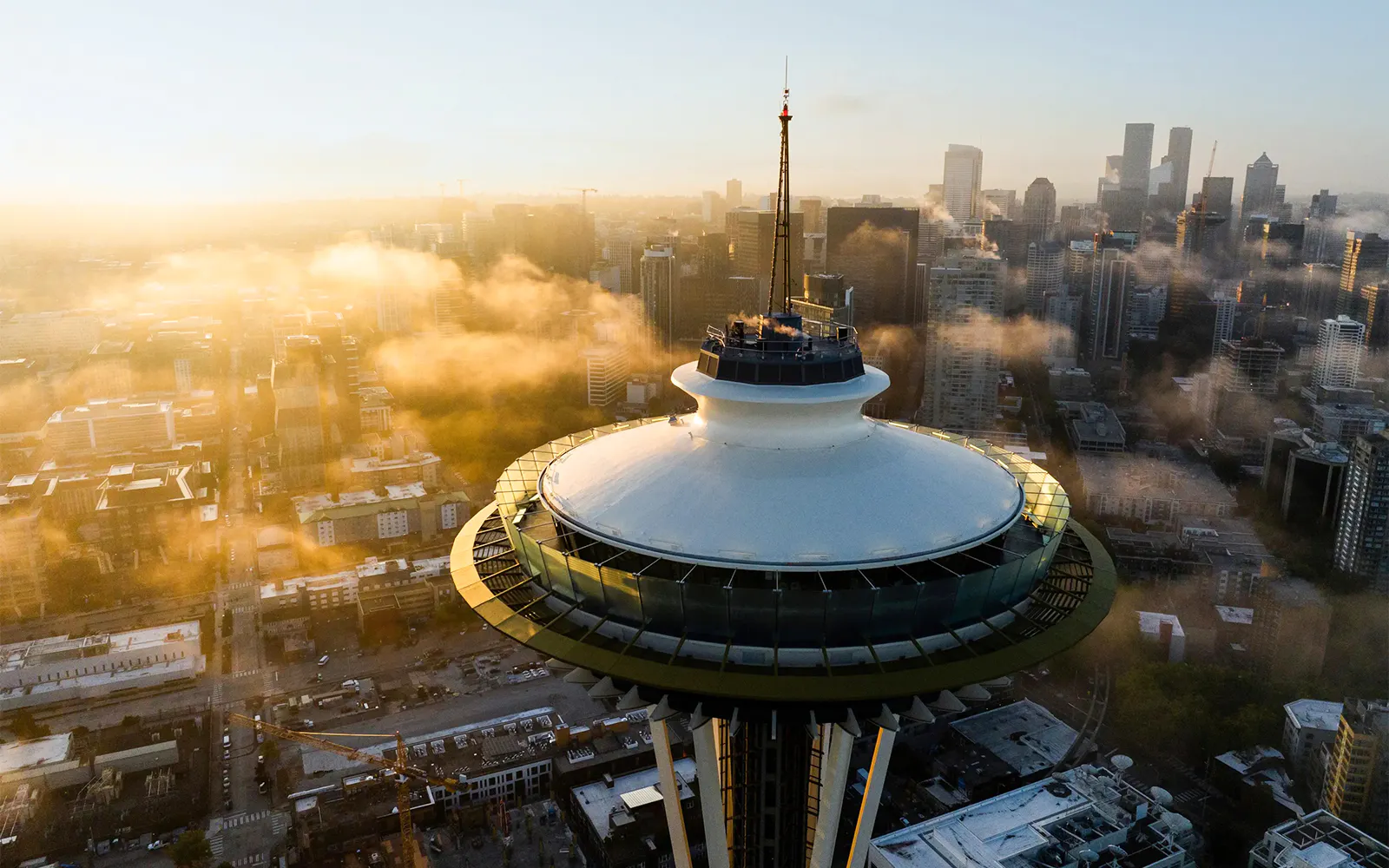 Seattle's Space Needle surrounded by cityscape and clouds during sunset.