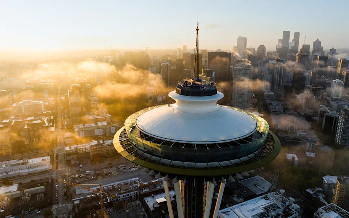 Seattle's Space Needle surrounded by cityscape and clouds during sunset.