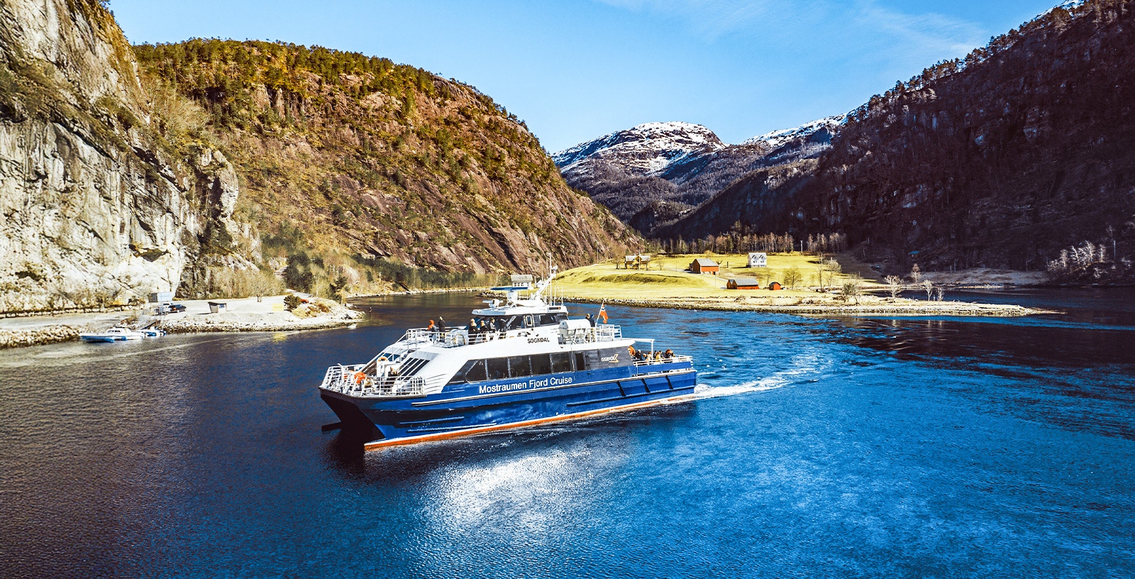 Mostraumen Fjord Cruise boat sailing through scenic Norwegian fjord with mountains in the background.