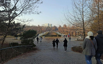 People walking in a park with trees and a distant building, Bucharest city exploration game.
