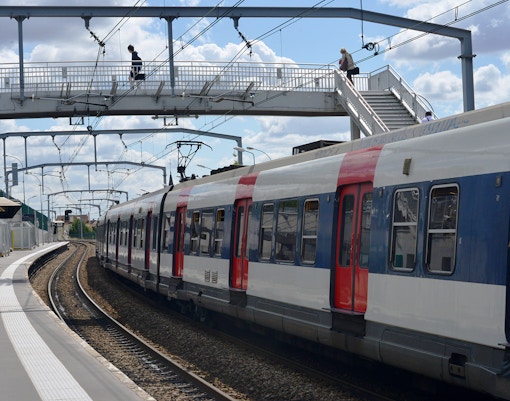 Paris RER train at a station with passengers on an overhead footbridge.