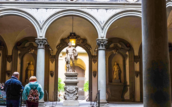 Statue in Accademia Gallery courtyard, Florence, with visitors observing.