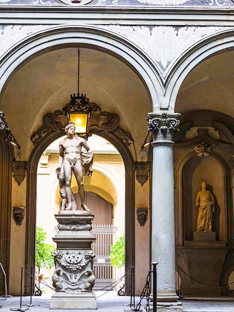 Statue in Accademia Gallery courtyard, Florence, with visitors observing.