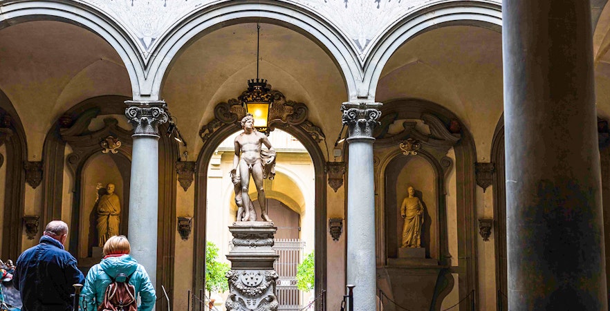 Statue in Accademia Gallery courtyard, Florence, with visitors observing.