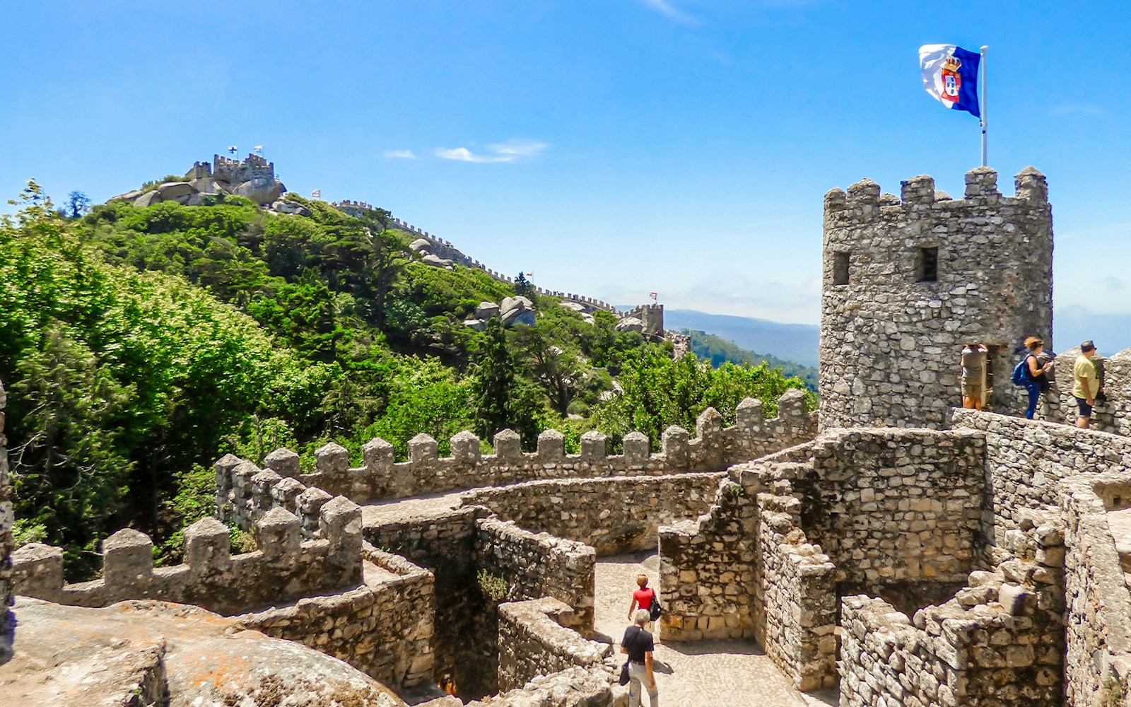 Moorish Castle walls with tourists, Pena Palace visible in the background, Sintra, Portugal.