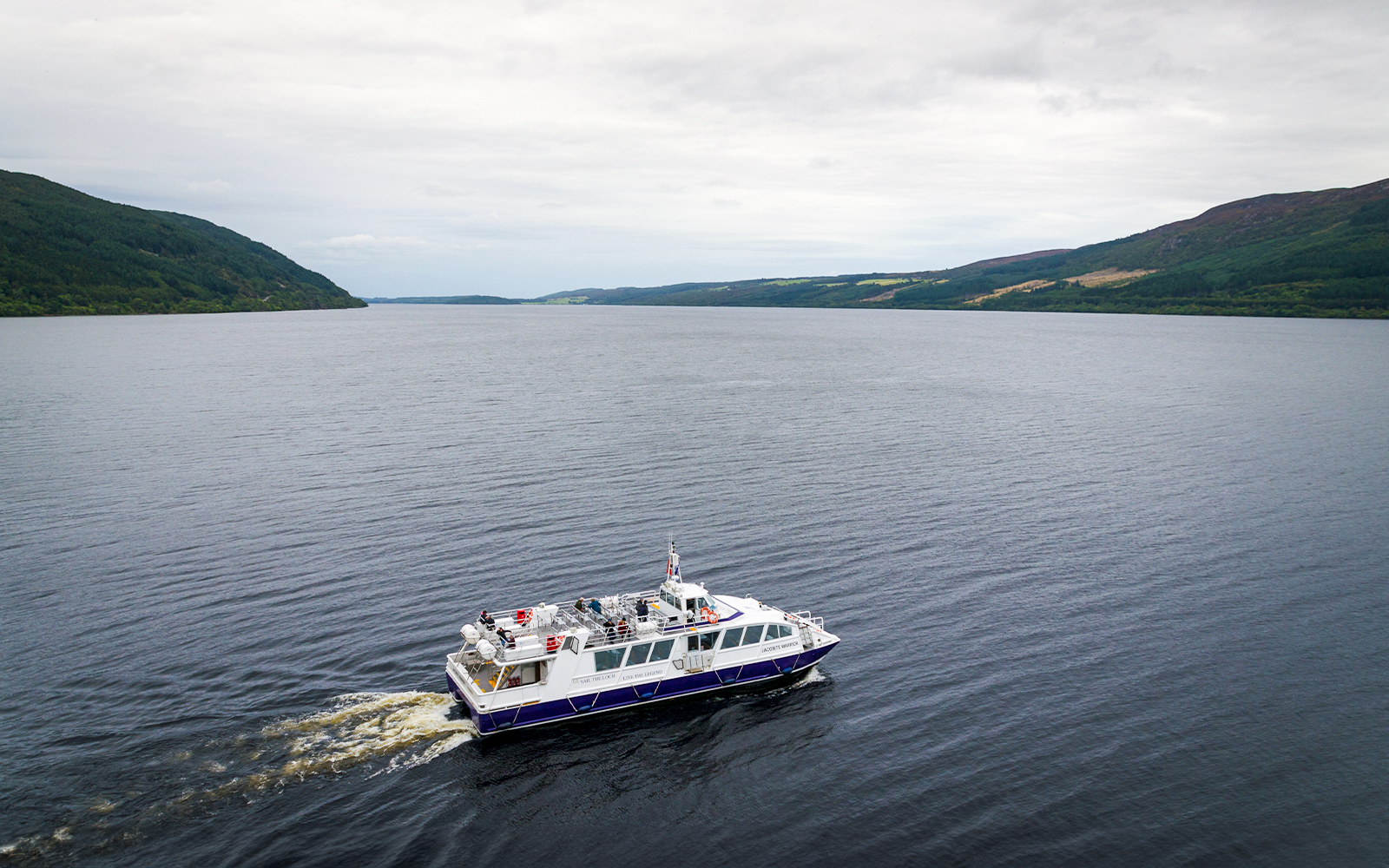 Tourist boat cruising on Loch Ness with scenic hills in the background.