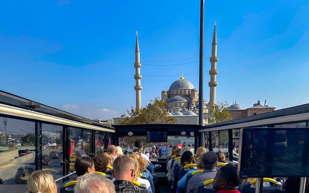 Open-top bus tour in Istanbul with view of a mosque's minarets in the background.