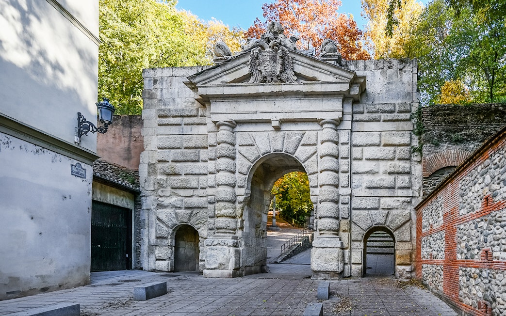 Gate of the Pomegranates entrance at Alhambra, Spain, with stone archway and surrounding trees.