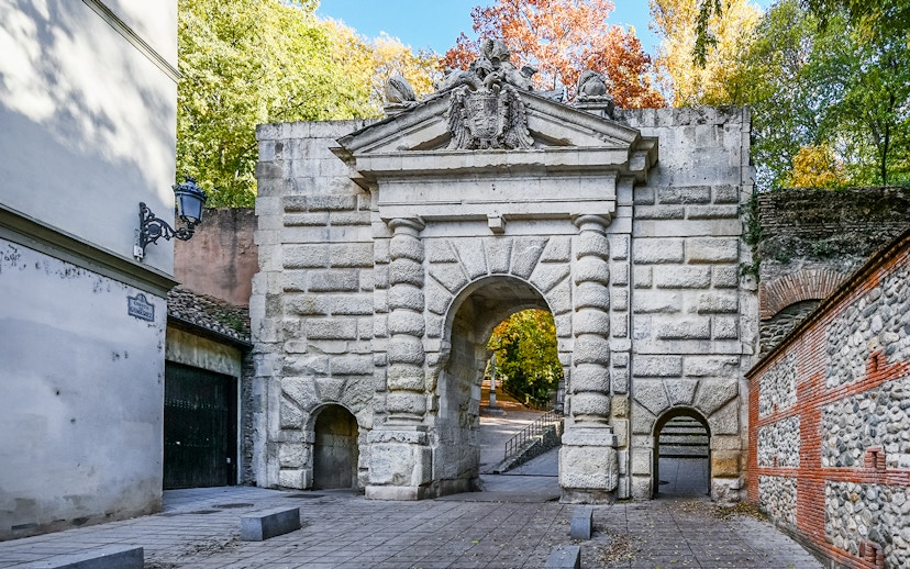 Gate of the Pomegranates entrance at Alhambra, Spain, with stone archway and surrounding trees.