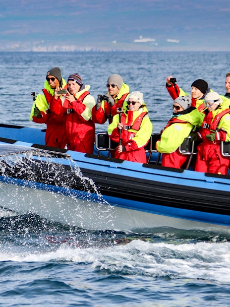 Guests photographing a whale's tail near a RIB speedboat on a Husavik whale watching tour.