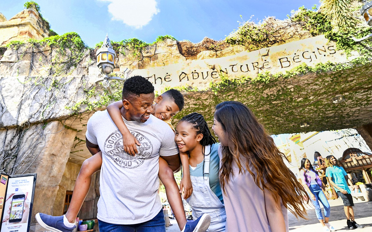 Family smiling under "The Adventure Begins" sign at Universal Studios Resort, Orlando.
