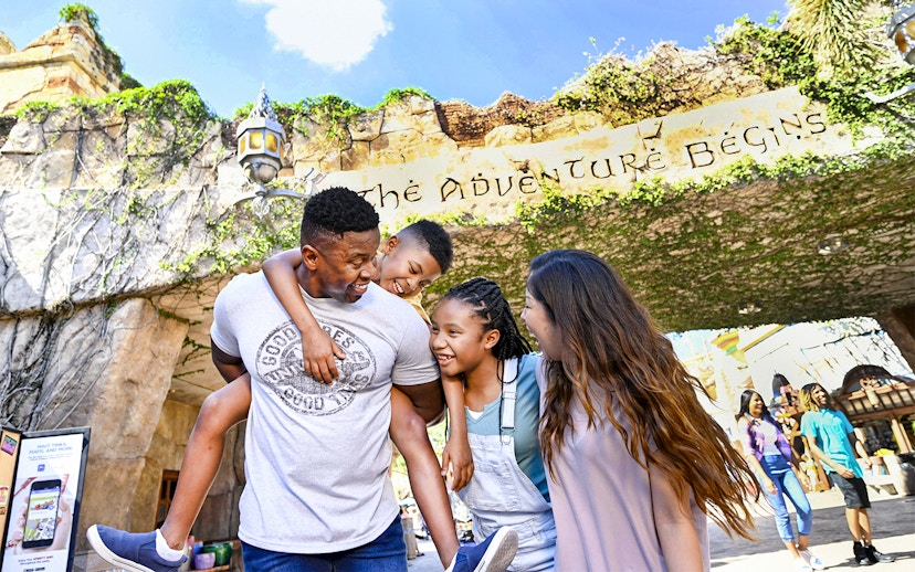Family smiling under "The Adventure Begins" sign at Universal Studios Resort, Orlando.