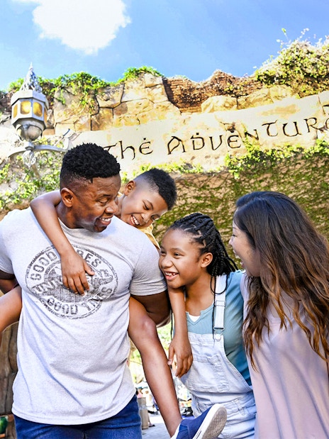 Family smiling under "The Adventure Begins" sign at Universal Studios Resort, Orlando.