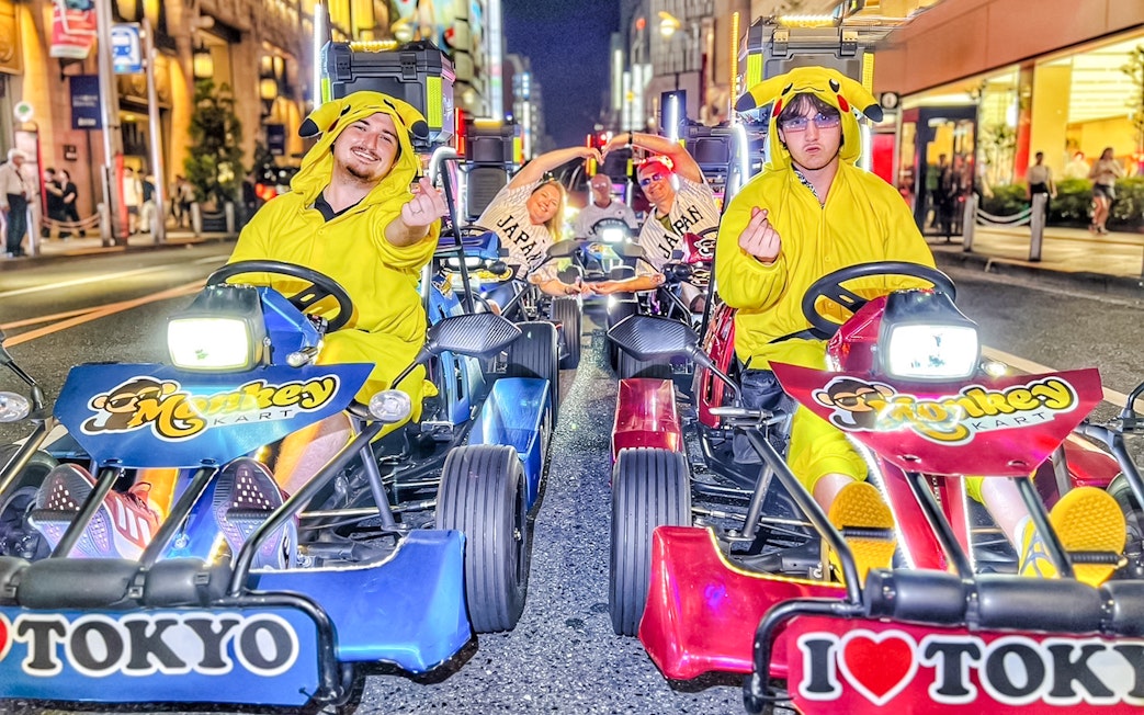 Tourists in Pikachu costumes driving go-karts on a Tokyo street at night.