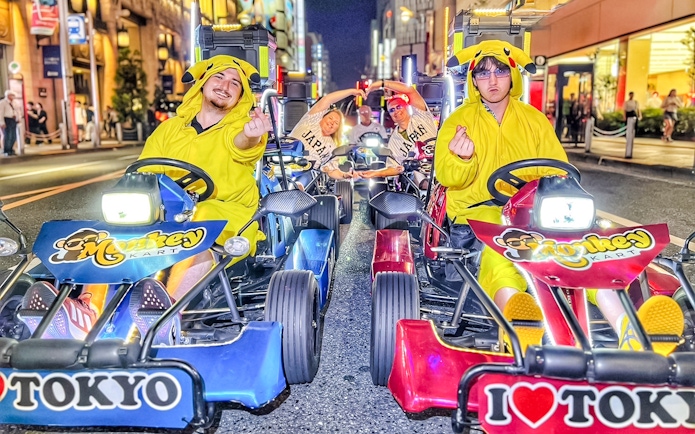 Tourists in Pikachu costumes driving go-karts on a Tokyo street at night.