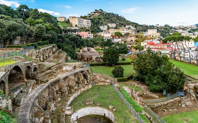 Ruins and greenery at the Archaeological Park of the Baths of Baiae, Italy, with hillside view.