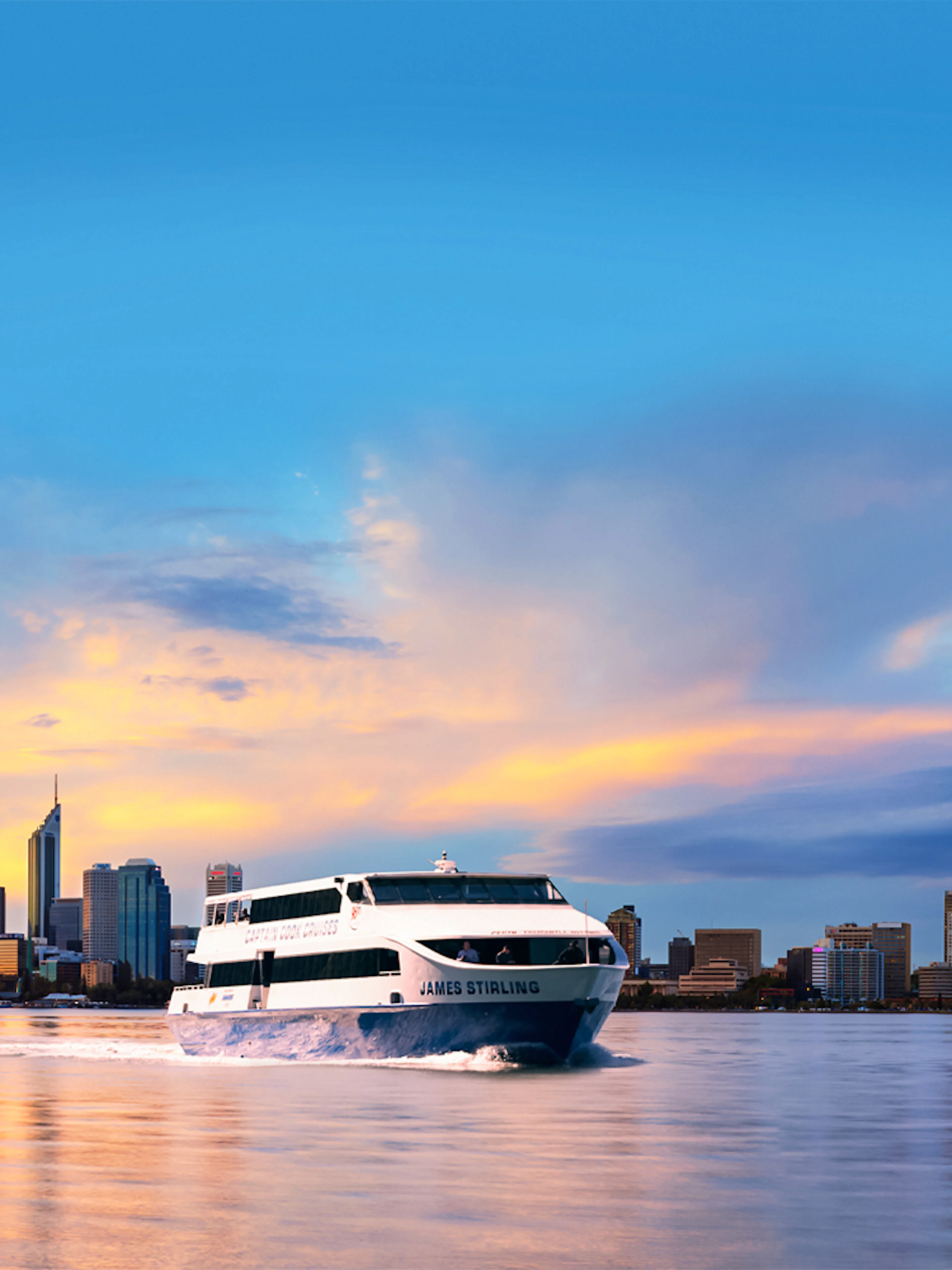 Cruise boat on Swan River with Perth city skyline at sunset.