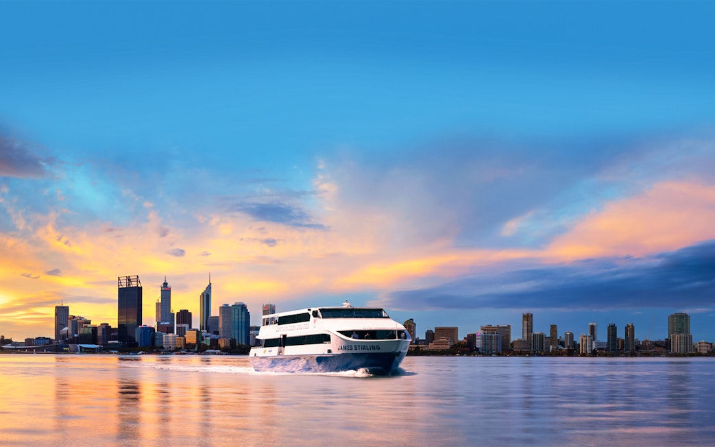 Cruise boat on Swan River with Perth city skyline at sunset.