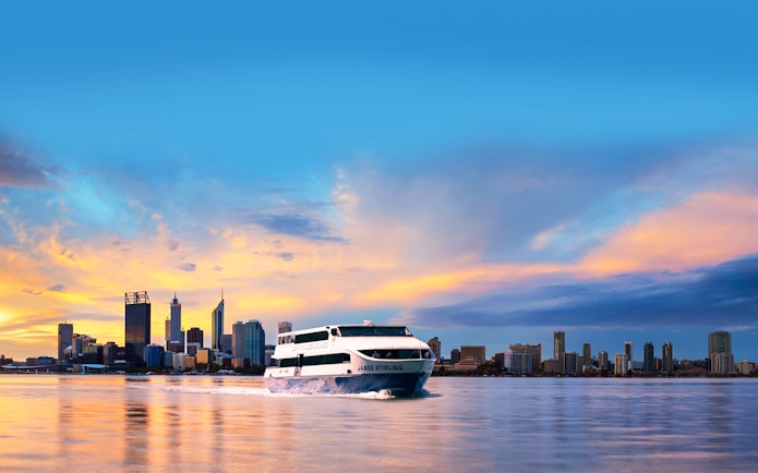 Cruise boat on Swan River with Perth city skyline at sunset.