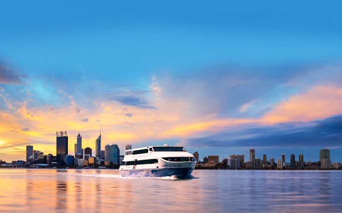 Cruise boat on Swan River with Perth city skyline at sunset.