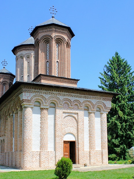 Exterior view of Snagov Monastery, Romania, featuring brick architecture and lush greenery.