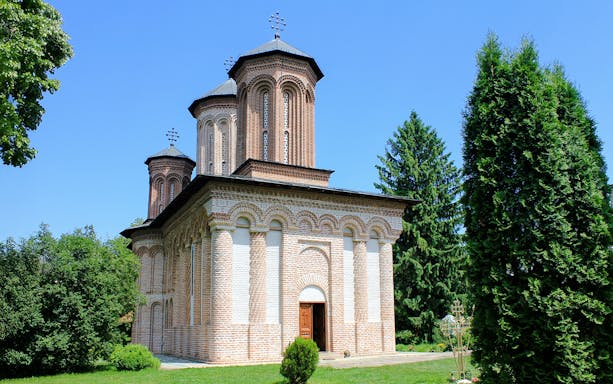 Exterior view of Snagov Monastery, Romania, featuring brick architecture and lush greenery.