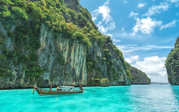 Speedboat near limestone cliffs on Phi Phi Island, Thailand, with turquoise water.